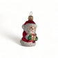 Suspension en verre soufflé, chromée et peinte à la main en forme de père Noël vêtu de son habit rouge, de gants verts et portant un cadeau doré serti d'un nœud rouge. La fourrure de son habit et de son bonnet est représenté en paillettes blanches.