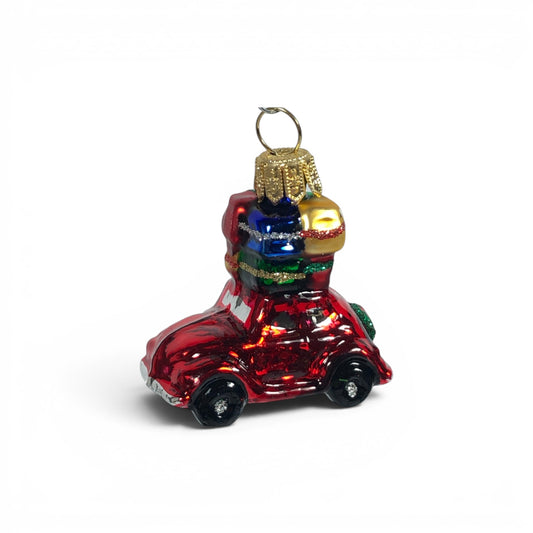 Suspension de Noël en verre soufflé, chromée et peinte à la main en forme de voiture rouge avec des paquets cadeaux rouge, or, bleu et vert sur son toit et une couronne de Noël accrochée à l'arrière sur le coffre.