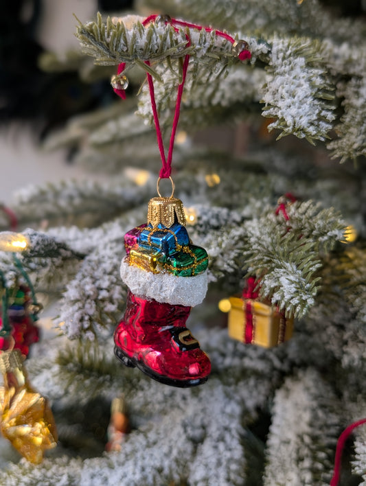 Suspension en verre soufflé, chromée et peinte à la main en forme de botte du Père Noël remplie de paquets cadeaux colorés vert, bleu, rose et doré. La fourrure de la botte est représentée par des paillettes blanches.