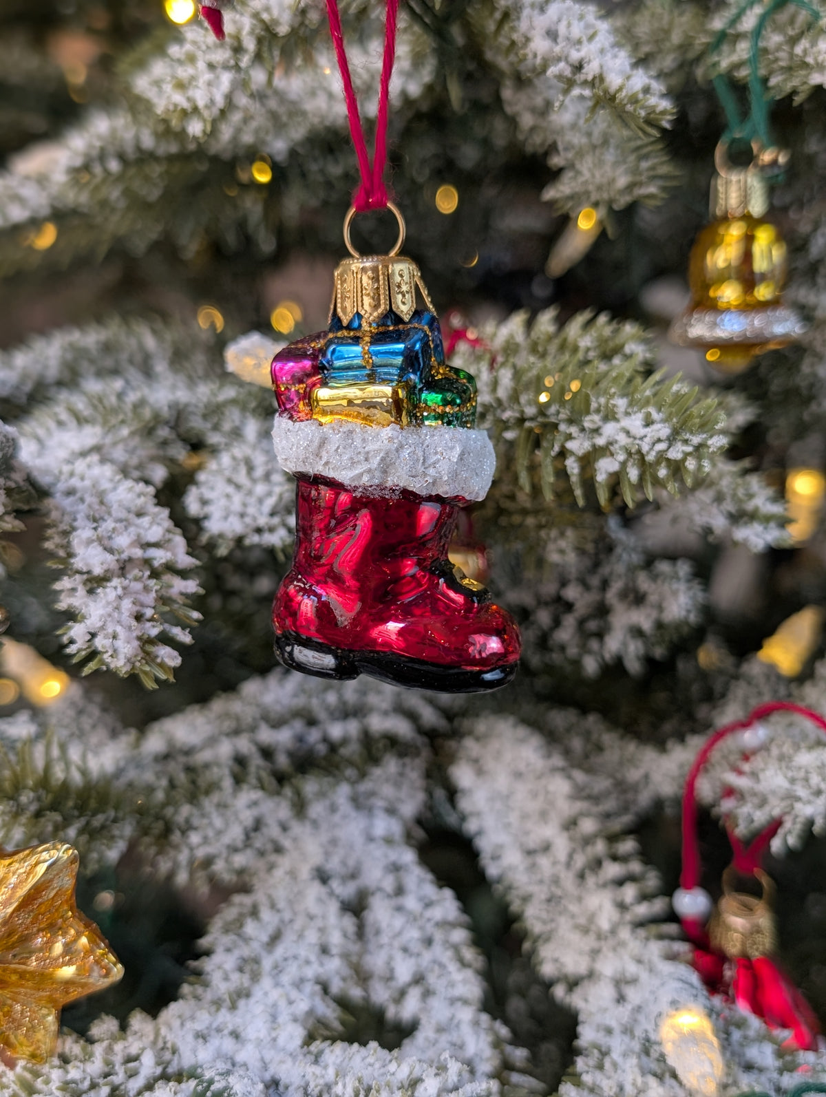 Suspension en verre soufflé, chromée et peinte à la main en forme de botte du Père Noël remplie de paquets cadeaux colorés vert, bleu, rose et doré. La fourrure de la botte est représentée par des paillettes blanches.
