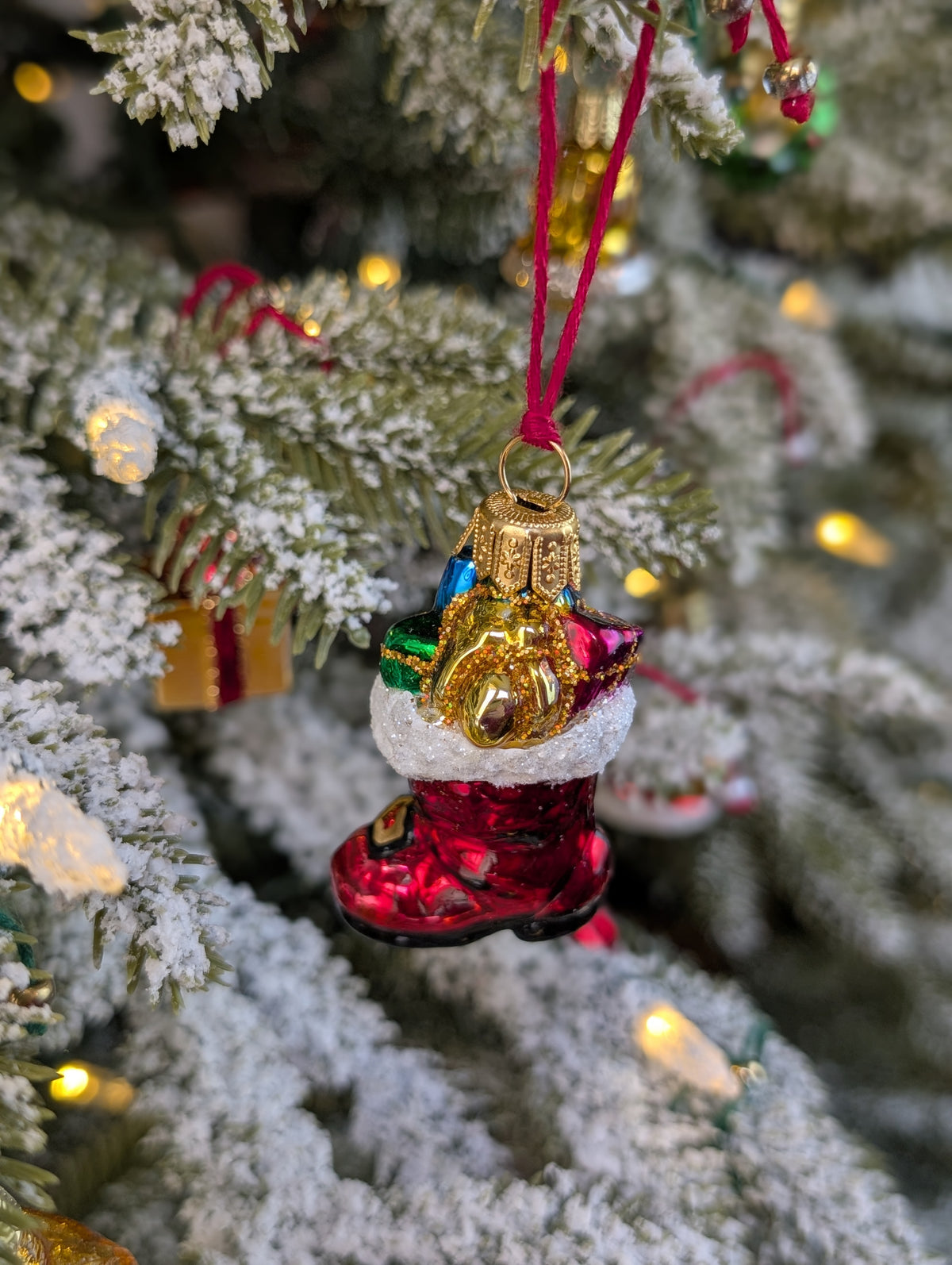 Suspension en verre soufflé, chromée et peinte à la main en forme de botte du Père Noël remplie de paquets cadeaux colorés vert, bleu, rose et doré. La fourrure de la botte est représentée par des paillettes blanches.