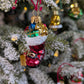 Suspension en verre soufflé, chromée et peinte à la main en forme de botte du Père Noël remplie de paquets cadeaux colorés vert, bleu, rose et doré. La fourrure de la botte est représentée par des paillettes blanches.
