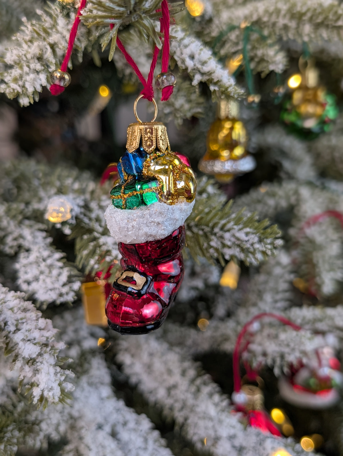Suspension en verre soufflé, chromée et peinte à la main en forme de botte du Père Noël remplie de paquets cadeaux colorés vert, bleu, rose et doré. La fourrure de la botte est représentée par des paillettes blanches.