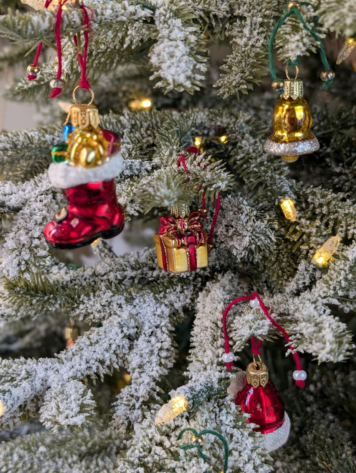 Suspensions de Noël en verre soufflé, chromées et peintes à la main en forme de paquet cadeau doré avec un ruban et nœud rouge, de botte du père Noël rouge garnie de cadeaux, d'une cloche dorée avec des paillettes argentées.