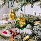 Suspension en verre soufflé, chromée et peinte à la main en forme de couronne de Noël verte décorée de boules de Noël rouges, de points de paillettes dorés et sertie d'un nœud doré. Suspensions en verre soufflé, chromées et peintes à la main en forme de cloche dorée et de paquet cadeau doré serti d'un ruban et nœud rouges.
