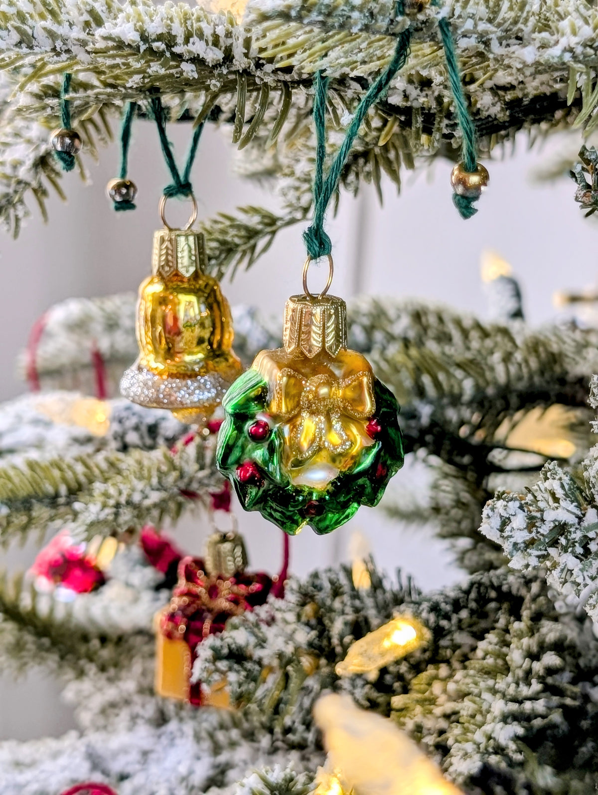 Suspension en verre soufflé, chromée et peinte à la main en forme de couronne de Noël verte décorée de boules de Noël rouges, de points de paillettes dorés et sertie d'un nœud doré. Suspensions en verre soufflé, chromées et peintes à la main en forme de cloche dorée et de paquet cadeau doré serti d'un ruban et nœud rouges.