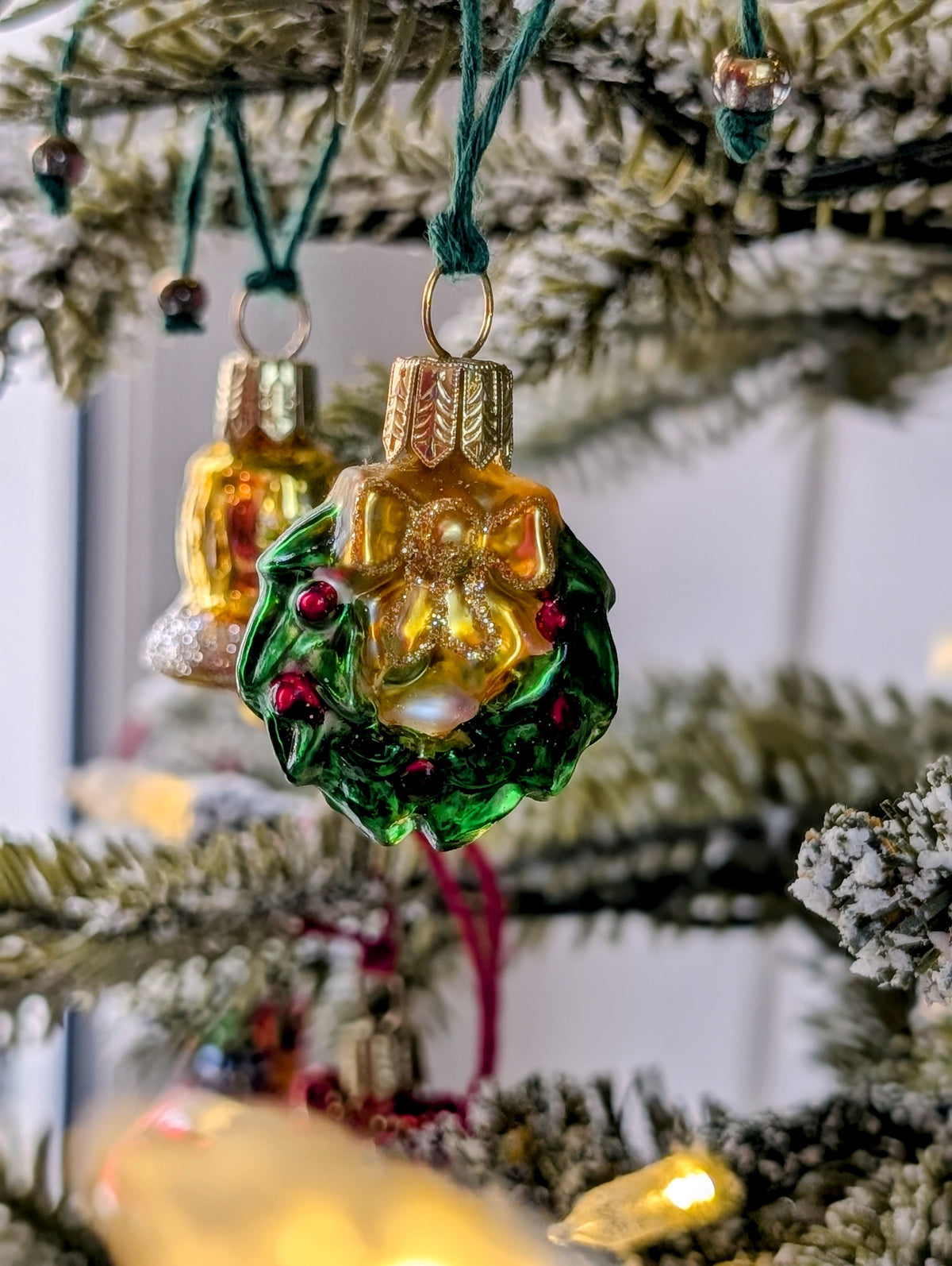 Suspension en verre soufflé, chromée et peinte à la main en forme de couronne de Noël verte décorée de boules de Noël rouges, de points de paillettes dorés et sertie d'un nœud doré. 