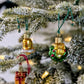 Suspension en verre soufflé, chromée et peinte à la main en forme de couronne de Noël verte décorée de boules de Noël rouges, de points de paillettes dorés et sertie d'un nœud doré. Suspensions en verre soufflé, chromées et peintes à la main en forme de cloche dorée et de paquet cadeau doré serti d'un ruban et nœud rouges.