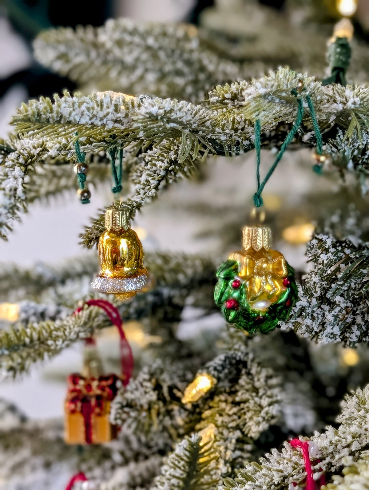 Suspension en verre soufflé, chromée et peinte à la main en forme de couronne de Noël verte décorée de boules de Noël rouges, de points de paillettes dorés et sertie d'un nœud doré. Suspensions en verre soufflé, chromées et peintes à la main en forme de cloche dorée et de paquet cadeau doré serti d'un ruban et nœud rouges.