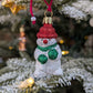 Suspension de Noël en verre soufflé puis pailleté en forme de bonhomme de neige avec un bonnet et nez rouges et une écharpe et des gants verts. 