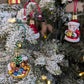 Suspension en verre soufflé, chromée et peinte à la main en forme de cheval à bascule avec une crinière blanche et une selle noire. Il a des paquets cadeaux entre les pattes et un sapin décoré d'une guirlande dorée sur le dos. Suspensions en verre soufflé, chromée et peintes à la main en forme de père Noël et de paquet cadeaux doré serti d'un ruban et nœud rouge.