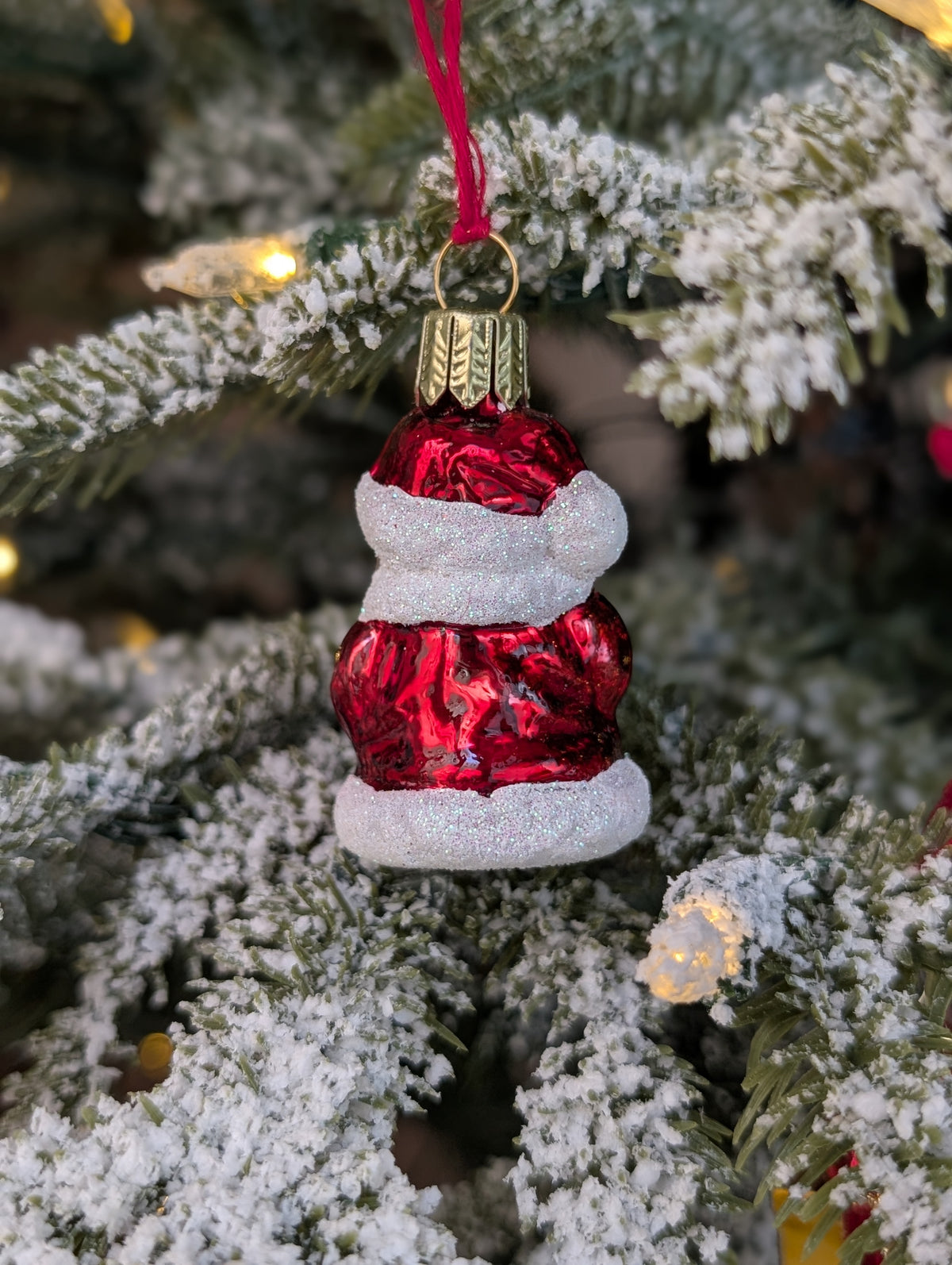 Dos de la suspension en verre soufflé, chromée et peinte à la main en forme de père Noël vêtu de son habit rouge. La fourrure de son habit et de son bonnet est représenté en paillettes blanches.