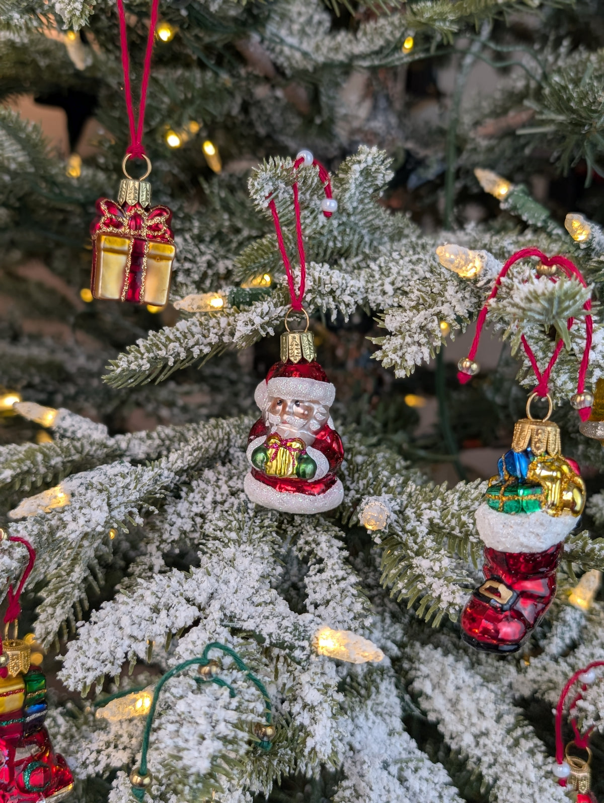 Suspensions en verre soufflé, chromées et peintes à la main en forme de père Noël vêtu de son habit rouge, de gants verts et portant un cadeau doré serti d'un nœud rouge, de paquet cadeau doré serti d'un ruban et nœud rouge, d'une botte du père Noël remplie de paquets cadeaux.