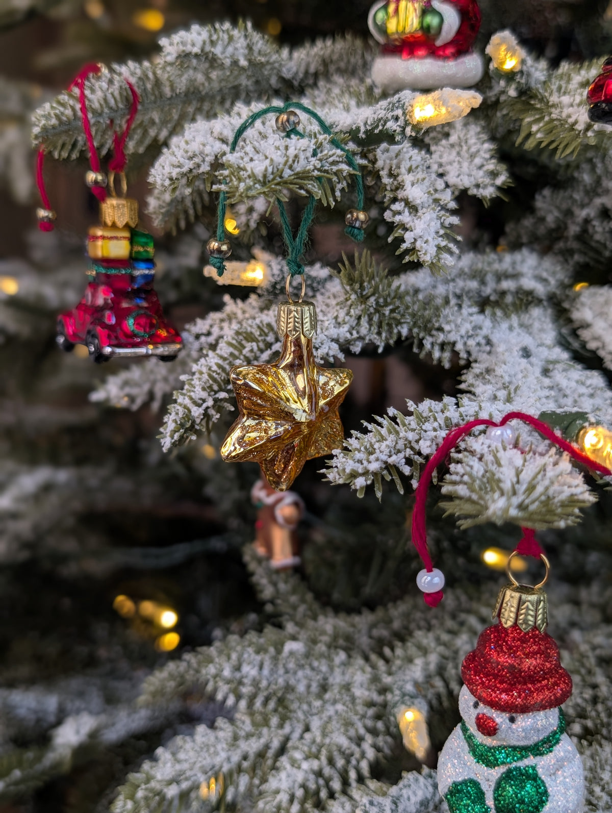 Suspensions en verre soufflé, chromées et peintes à la main en forme d'étoile à six branches dorée, de voiture rouge avec des paquets cadeaux sur le toit, d'un bonhomme de neige avec un bonnet rouge, une écharpe et des gants verts.