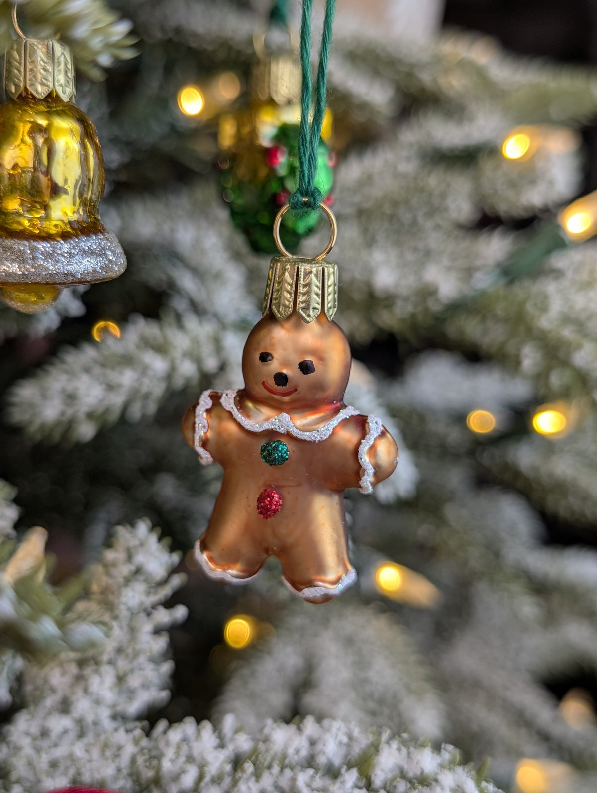 Suspension de Noël en verre soufflé, chromée et peinte à la main en forme de bonhomme en pain d'épices avec ses deux boutons de vêtement, un rouge et un vert, en paillettes. Suspension de Noël en verre soufflé, chromée et peinte à la main en forme de cloche dorée et paillettes argentées.