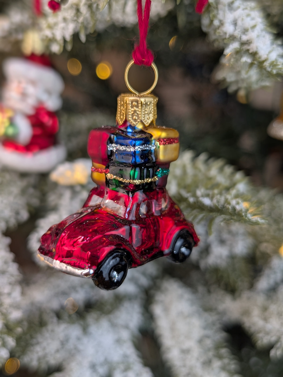 Suspension de Noël en verre soufflé, chromée et peinte à la main en forme de voiture rouge avec des paquets cadeaux rouge, or, bleu et vert sur son toit.