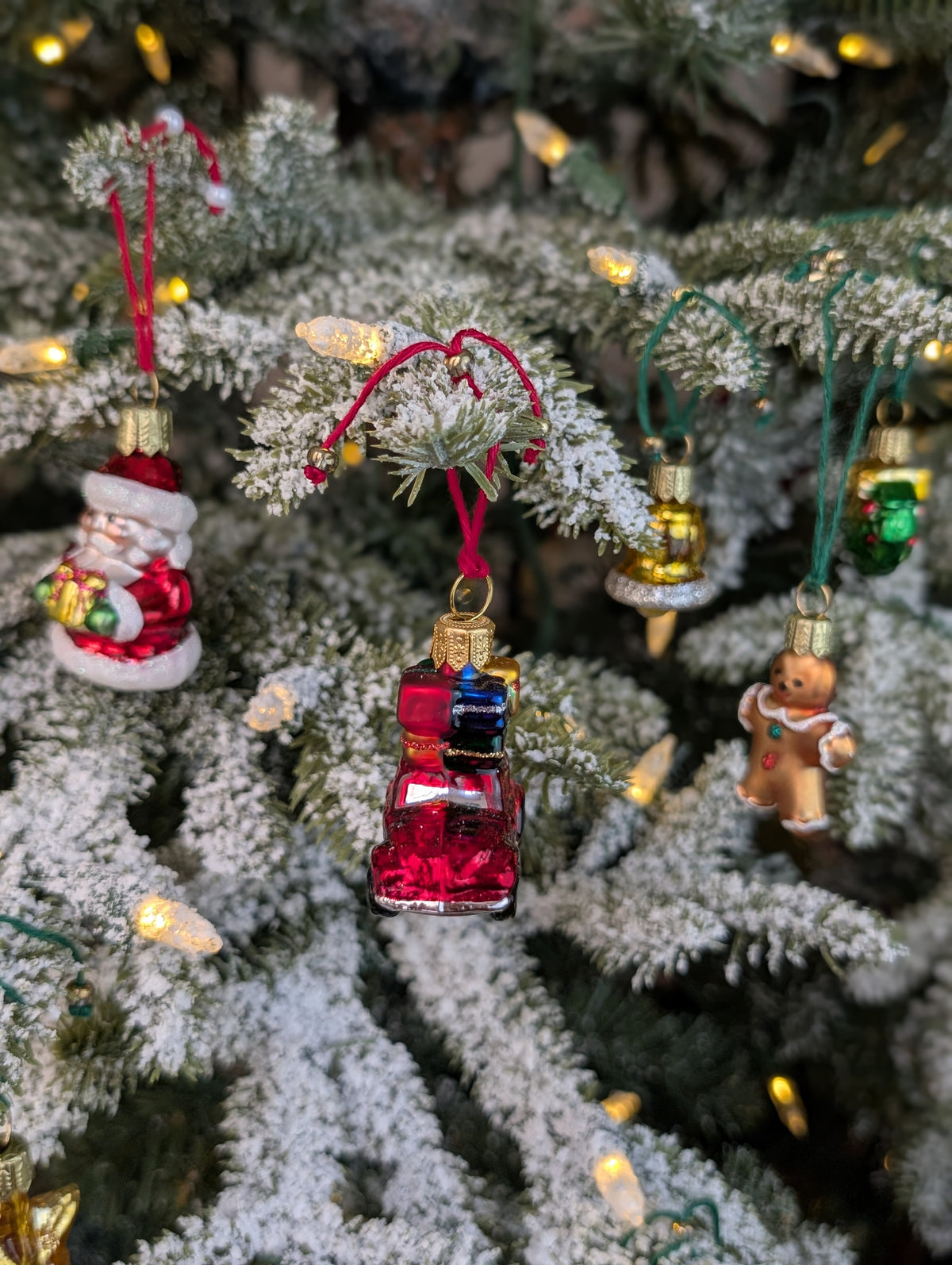 Suspensions de Noël en verre soufflé, chromées et peintes à la main en forme de voiture rouge avec des paquets cadeaux, de père noël tenant un cadeau, de bonhomme en pain d'épice, de cloche dorée et de couronne de noël verte.