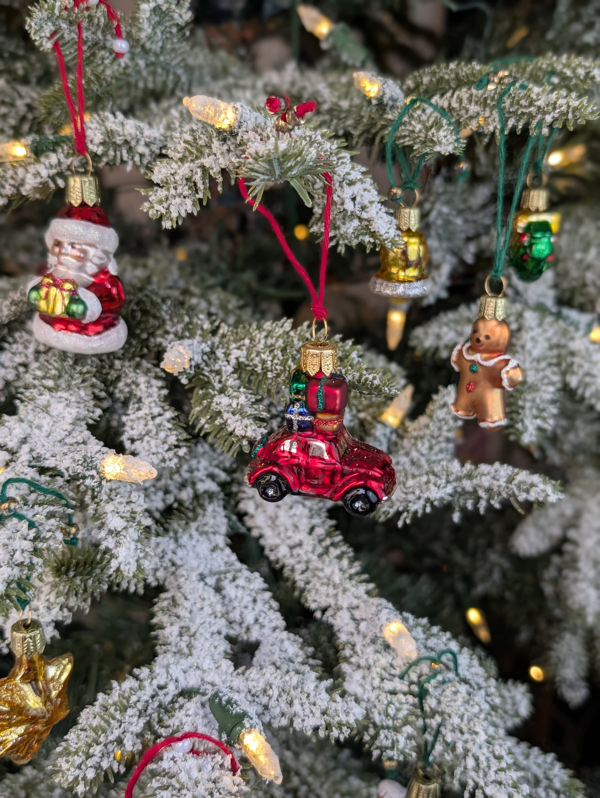 Suspensions de Noël en verre soufflé, chromées et peintes à la main en forme de voiture rouge avec des paquets cadeaux, de père noël tenant un cadeau, de bonhomme en pain d'épice, de cloche dorée, d'étoile dorée et de couronne de noël verte.
