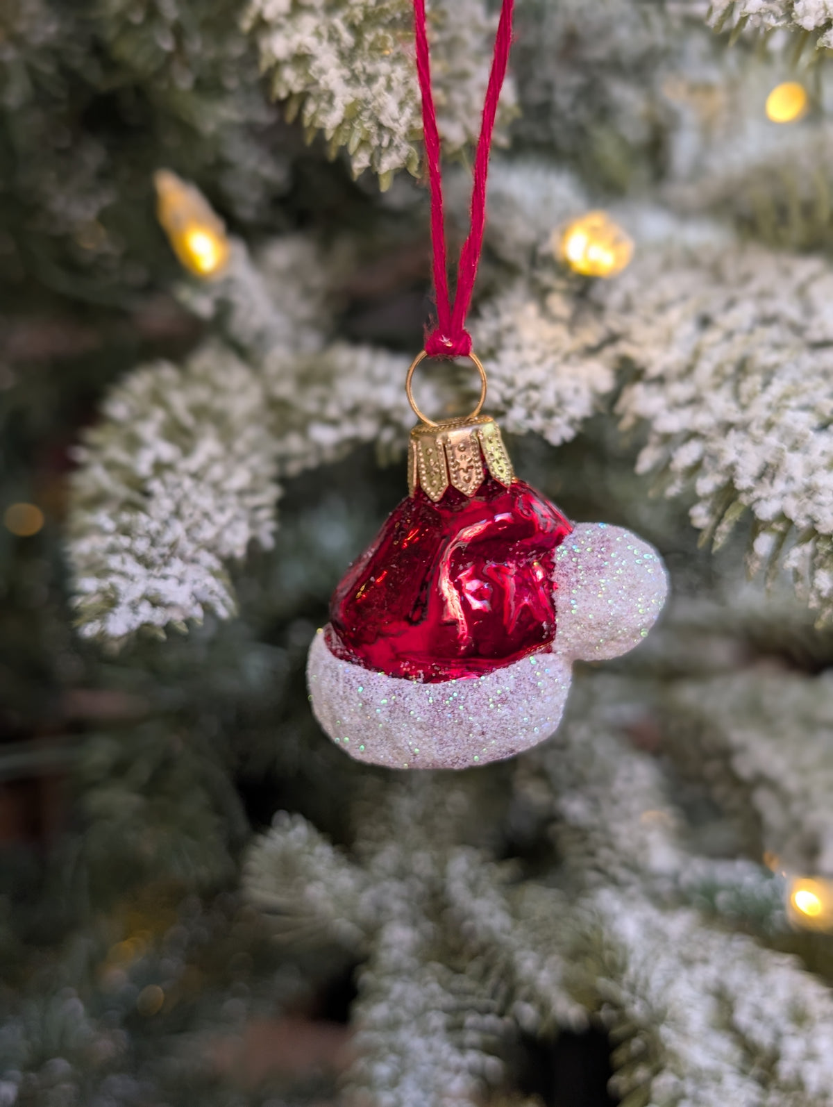 Suspension en verre soufflé, chromée et peinte à la main en forme de bonnet du Père Noël rouge vif, la fourrure est représentée par des paillettes blanches. 