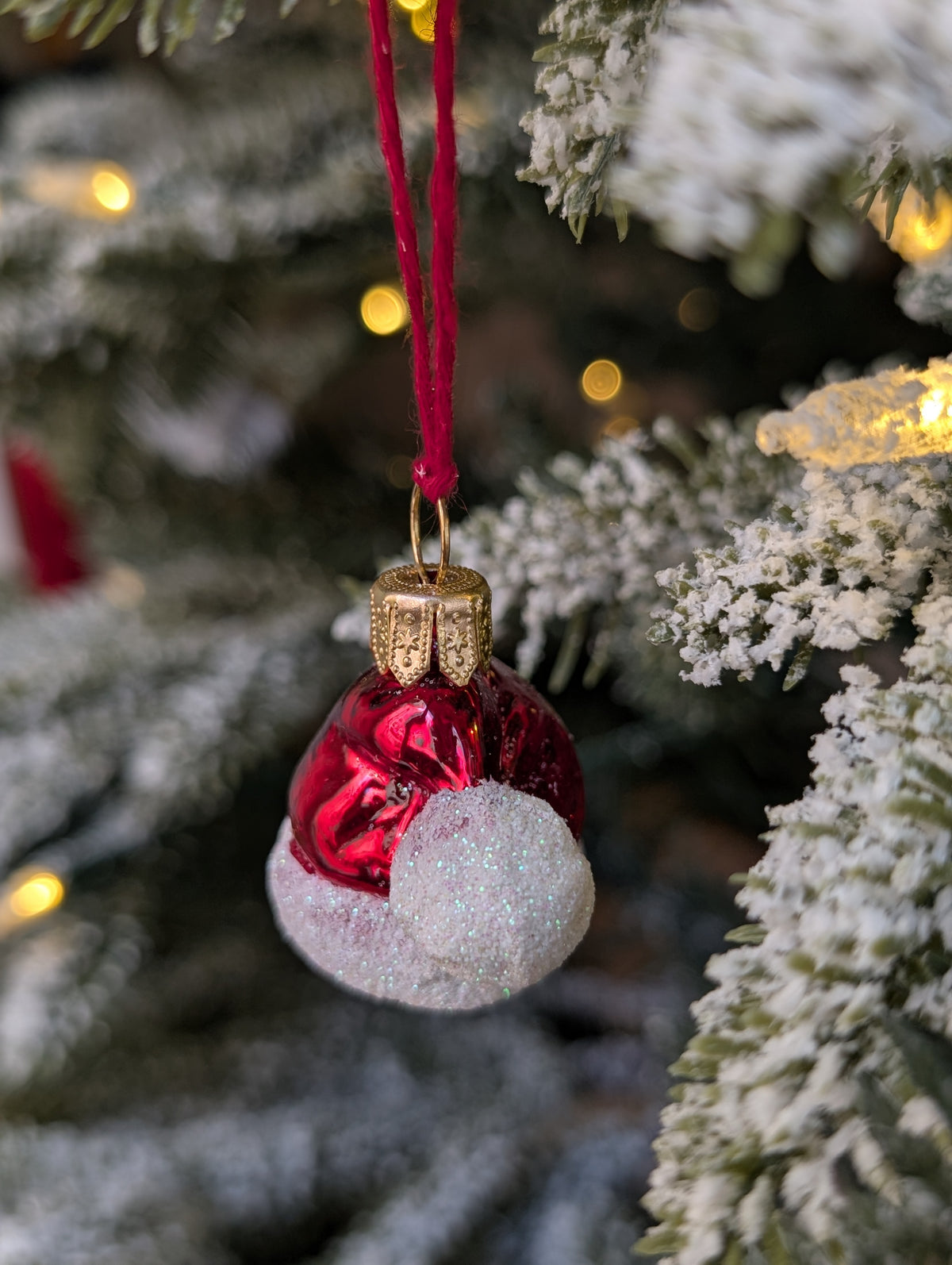 Suspension en verre soufflé, chromée et peinte à la main en forme de bonnet du Père Noël rouge vif, la fourrure est représentée par des paillettes blanches. 