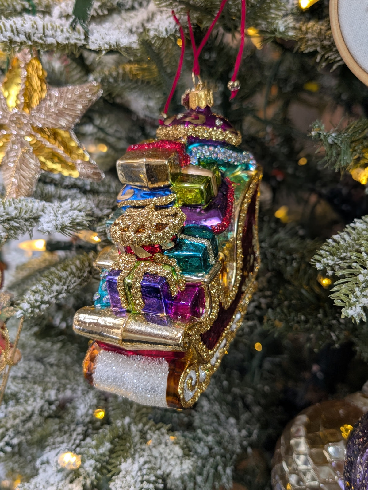 Suspension en forme de traineau du père Noël rouge et doré, garni de paquets cadeaux multicolores. 