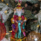 Suspension en forme des trois rois mages apportant leurs cadeaux. ils sont habillés de riches couleurs et chapeaux et sont posés sur un socle doré décoré de houx et baies rouges. Vue sur Melchior de face apportant l'or et Gaspard de profil apportant l'encens et Balthazar de profil offrant la myrrhe.