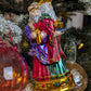Suspension en forme des trois rois mages apportant leurs cadeaux. ils sont habillés de riches couleurs et chapeaux et sont posés sur un socle doré décoré de houx et baies rouges. Vue sur Gaspard de face apportant l'encens et Melchior de profil apportant l'or.