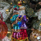 Suspension en forme des trois rois mages apportant leurs cadeaux. ils sont habillés de riches couleurs et chapeaux et sont posés sur un socle doré décoré de houx et baies rouges. Vue de Gaspard et Balthazar de dos.