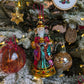 Suspension en forme des trois rois mages apportant leurs cadeaux. ils sont habillés de riches couleurs et chapeaux et sont posés sur un socle doré décoré de houx et baies rouges. Suspensions boules de noël  en verre style venise rouge et style ananas or. Suspension miniature en forme d'étoile dorée. Suspension broderie sapin décoré de bougies, étoile dorée au sommet et paquets cadeaux au pied du sapin. Suspension rondin de bois pyrogravé joyeux noël.