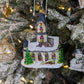 Suspension en forme d'église blanche, avec des vitraux colorés vert, jaune, bleu, violet et rouge et des rosaces dorées.  le toit bleu gris est enneigé et l'église est entourée de sapin verts