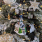 Suspension en forme d'église blanche, avec des vitraux colorés vert, jaune, bleu, violet et rouge et des rosaces dorée, son toit bleu gris est enneigé et l'église est entourée de sapin verts; étoile brodée de perles blanches et or ; cygne en feutrine avec des plumes blanches serties de perles et cristaux ; miniature en forme d'étoile dorée; boule de Noël crème décorée de feuilles de gui vertes et or avec des baies rouges ; cœur transparent volutes baroques or blanc et argent ; bonhomme de neige et son sapin
