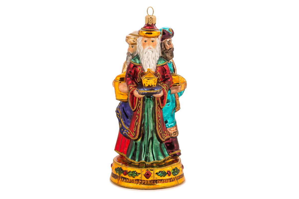 Suspension en forme des trois rois mages apportant leurs cadeaux. ils sont habillés de riches couleurs et chapeaux et sont posés sur un socle doré décoré de houx et baies rouges. Vue sur Melchior de face apportant l'or et Gaspard de profil apportant l'encens et Balthazar de profil offrant la myrrhe.