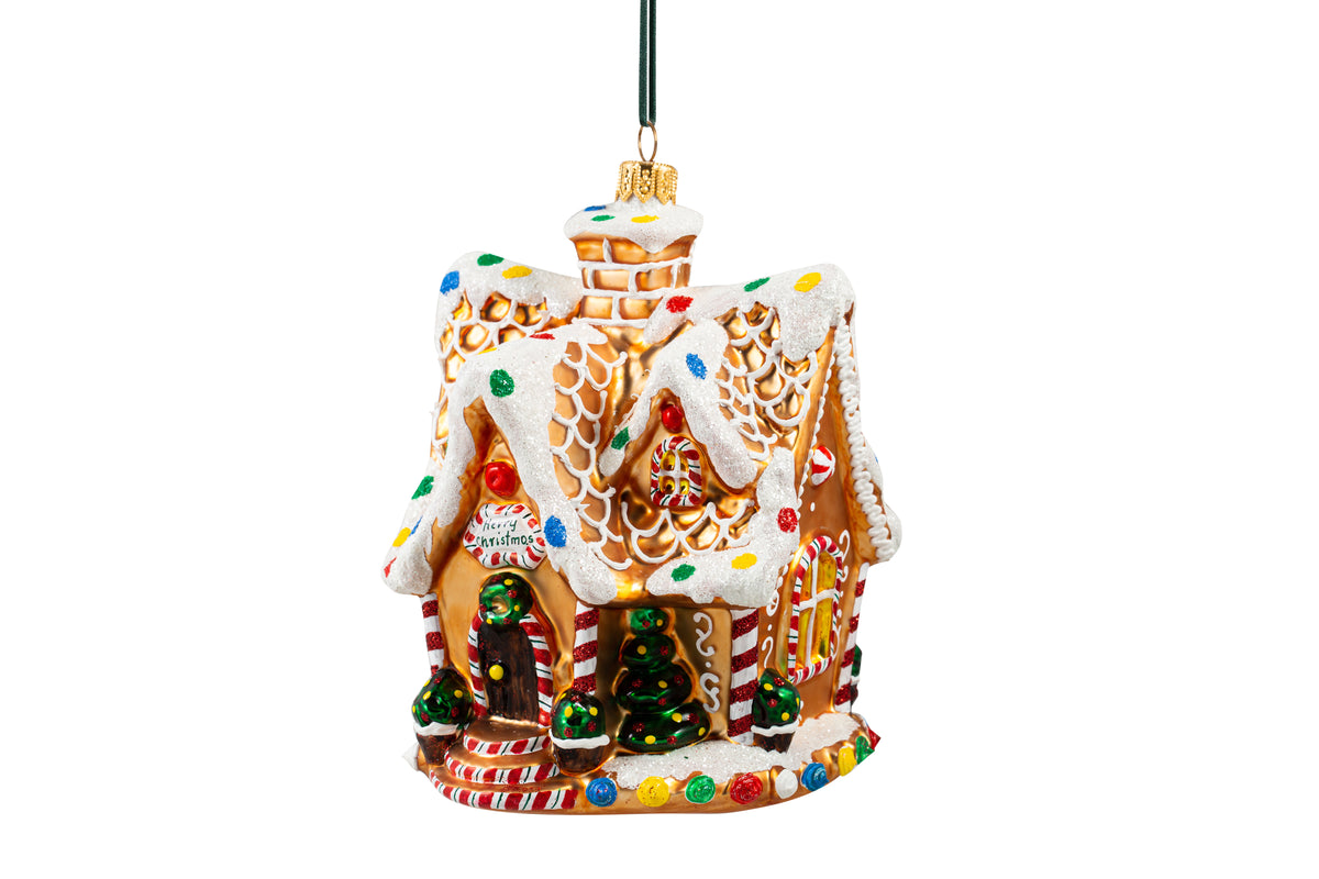 Suspension en forme de maison en pain d'épices décorée de glaçage blanc et de bonbons rouges, verts, bleus et jaunes. Joyeux Noël est écrit sur une pancarte au-dessus de la porte. 